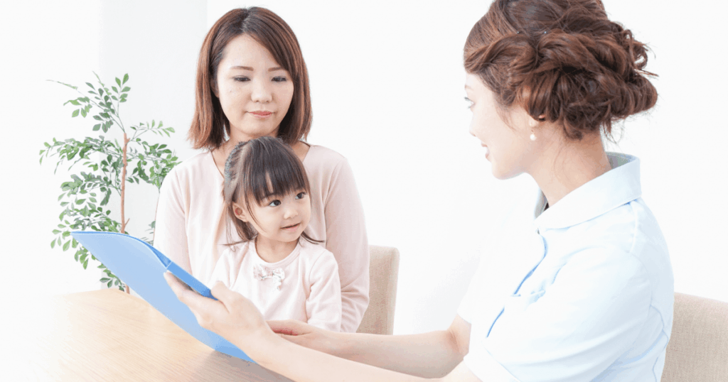 歯科スタッフが母親と子どもに説明をしている写真。歯並びを早めに確認する大切さを解説する記事内画像。